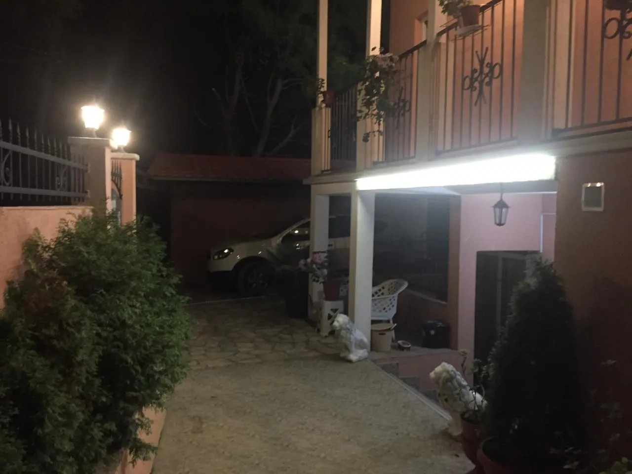 Night view of house facade with parked car, balcony, and stone pathway.