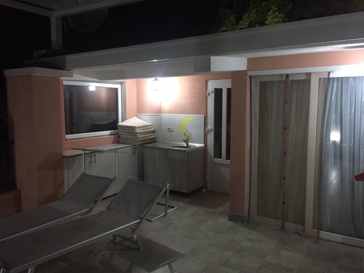 Terrace of a house in Shushan, Montenegro: summer kitchen, sun loungers, and panoramic glazing in the evening.