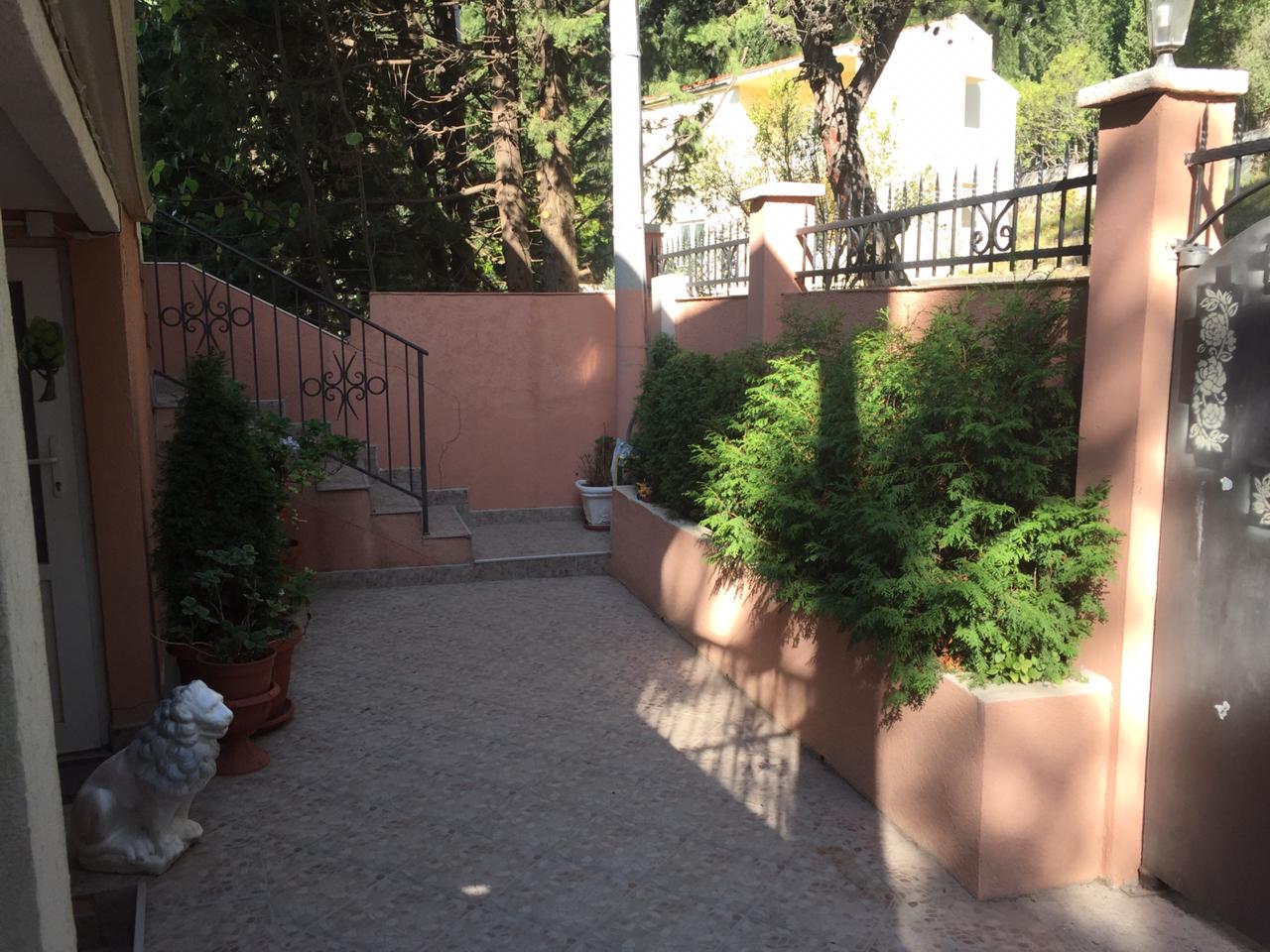 Cozy house courtyard in Shushan, Montenegro: paved area, decorative thuja trees, wrought-iron railings, and a lion statue.