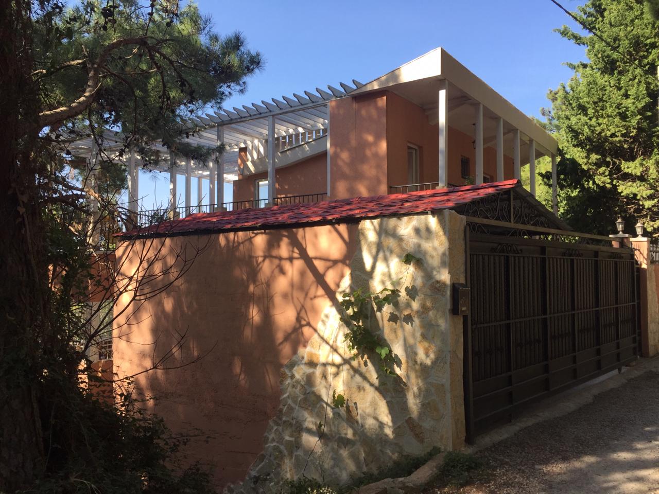 Two-story house in Shushan, Montenegro: facade with a terrace, pergola, and stone-clad fence by the entrance gate.