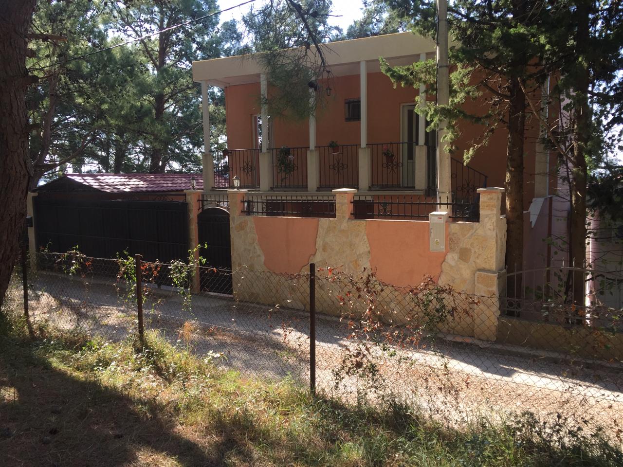 Two-story house with a terrace and stone fence surrounded by pine trees, Shushan, Montenegro. Front view of a private house.