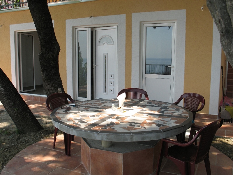 Terrace with a stone table by the house in Sutomore, Montenegro: sea view, tiled finish, and plastic furniture.