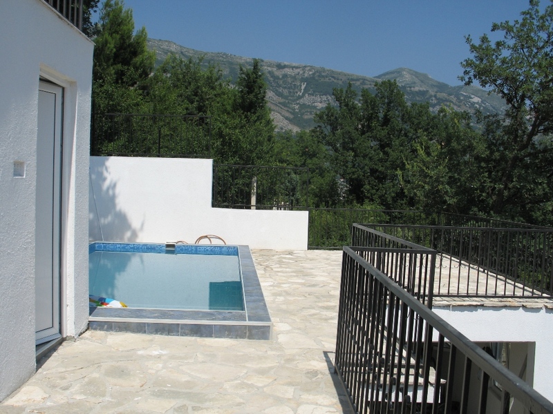 Terrace with a pool and mountain views by the house in Sutomore, Montenegro: stone finish, wrought-iron railings, and a garden.