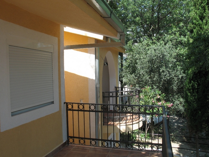 Balcony with wrought-iron railing and a view of the garden in a private house, Sutomore, Montenegro. Facade finished with yellow plaster.