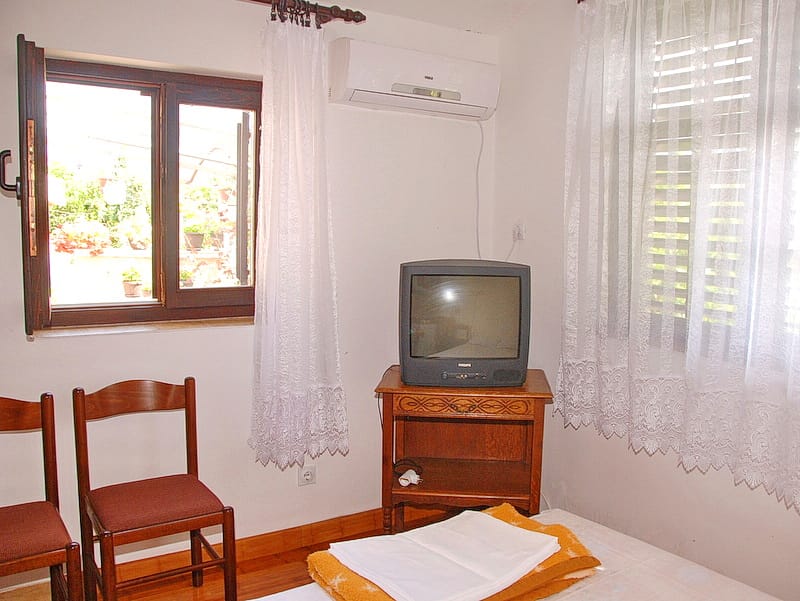 Bedroom in a house in Igalo, Montenegro: wooden chairs, TV stand, air conditioner, and a view of the terrace with plants.