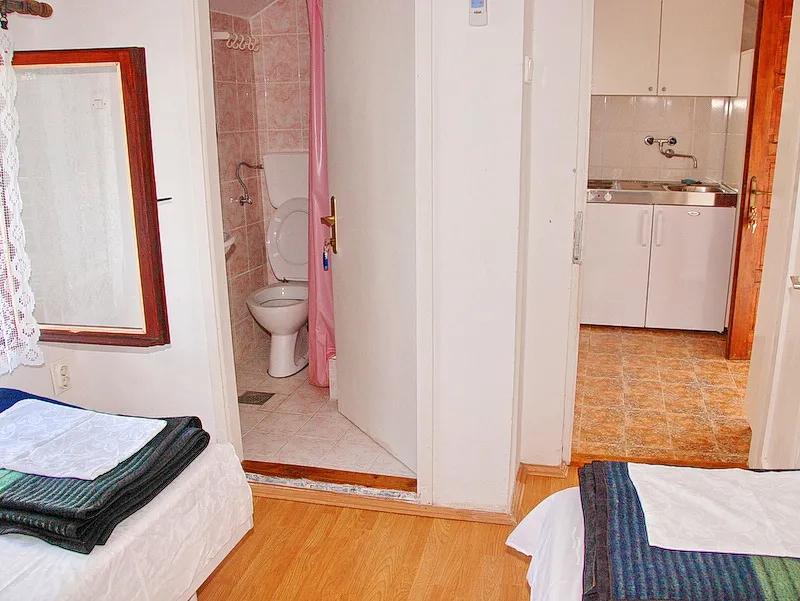 View of a bedroom with two beds, an open door to the toilet, and a glimpse of the kitchen.