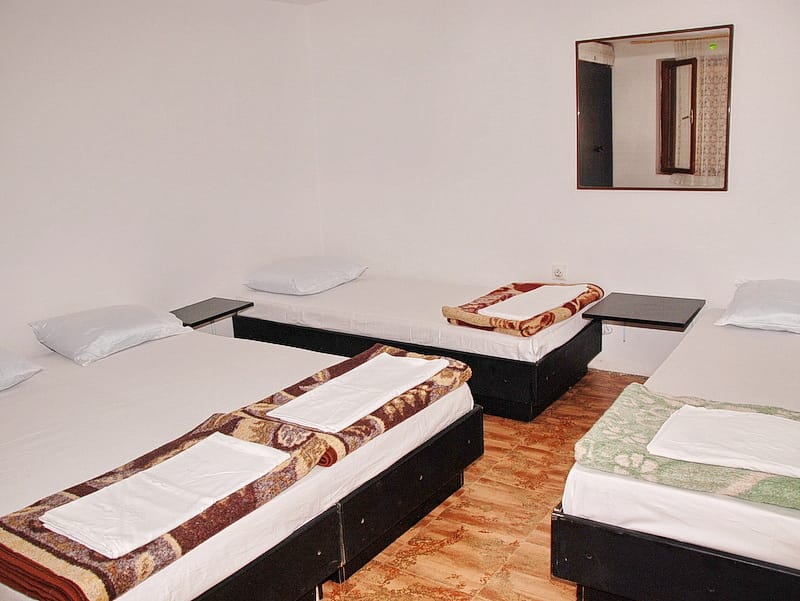 Triple bedroom in a house in Igalo, Montenegro: three beds with bedding, a wall mirror, and tiled flooring.
