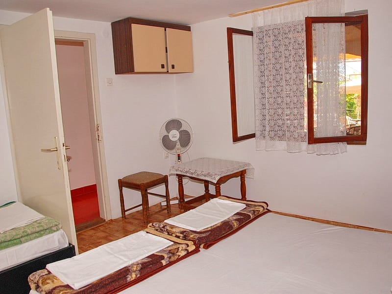 Bedroom in a house in Igalo, Montenegro: double bed, desk, chair, fan, and access to a private bathroom.