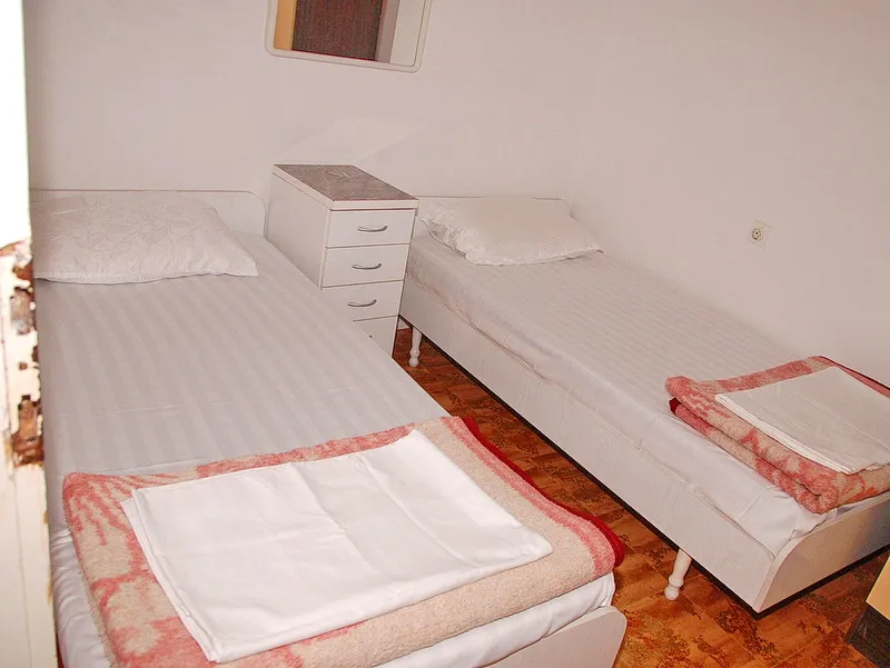 Two single beds with white bedding and a nightstand between them on a parquet floor.