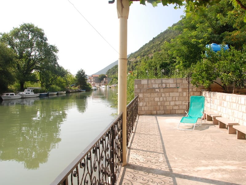 Terrace of a house in Igalo, Montenegro: view of the river with boats, stone masonry, a sun lounger, and a wrought-iron railing.