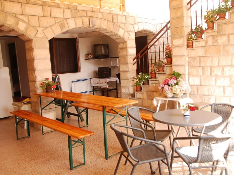 Covered terrace with stone arches and furniture in a house in Igalo, Montenegro: dining area, flowers, and staircase.