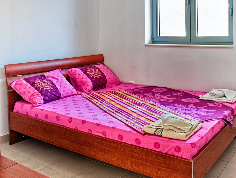 Bedroom with a double bed in an apartment in Petrovac, Montenegro: a bright room with tile flooring and a window.