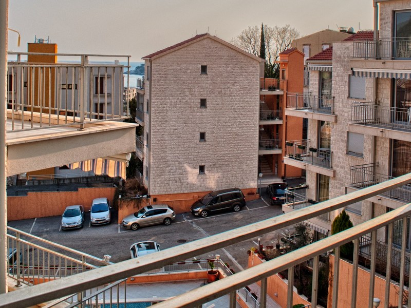 View from the apartment balcony in Petrovac, Montenegro: modern residential buildings, parking, and a sea view on the horizon.