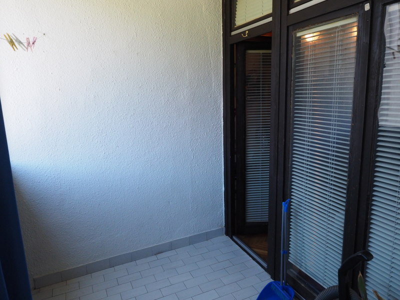 Open balcony with white finishes and access to the apartment in Bar, Montenegro, with dark door frames and shutters.