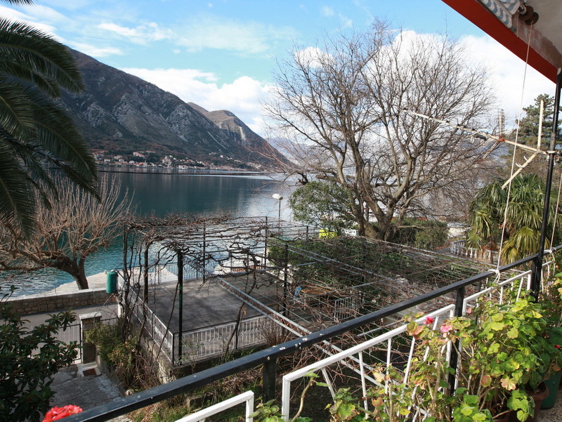 View from the balcony of a house in Dobrota, Montenegro: panorama of the Bay of Kotor, mountains, and a terrace with a vineyard.