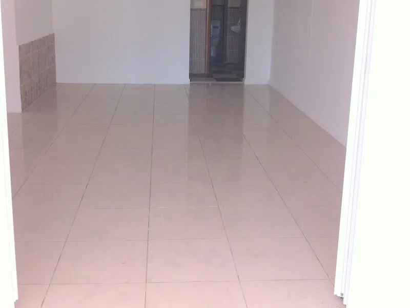 Empty room with light tiled flooring and white walls; a doorway leading to a bathroom is visible in the background.