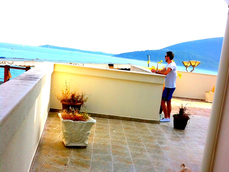 Spacious apartment terrace in Herceg Novi, Montenegro, with panoramic sea and mountain views, tiled floor, and plants.