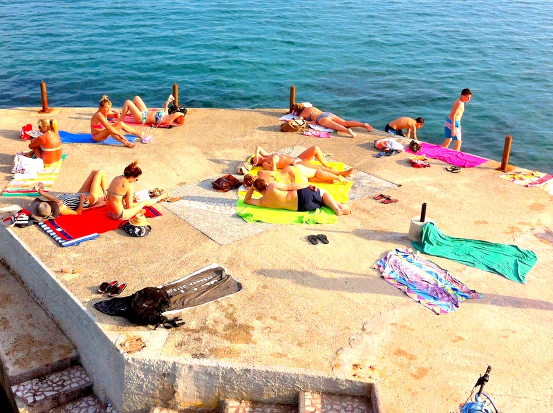 People sunbathe on a concrete pier by the sea in Herceg Novi, Montenegro, view of the beach near apartment No. 1135.