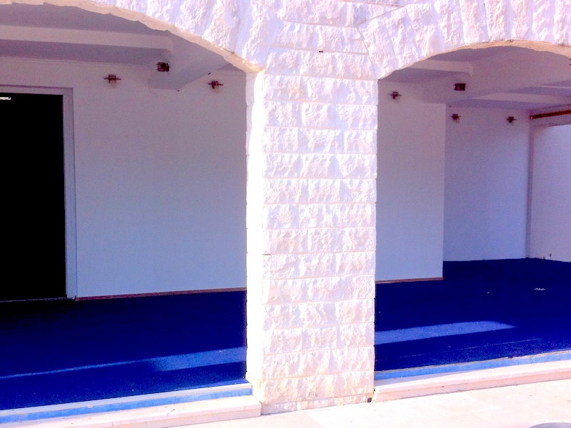 Apartment terrace in Herceg Novi, Montenegro: stone arches, light finishes, and blue flooring.
