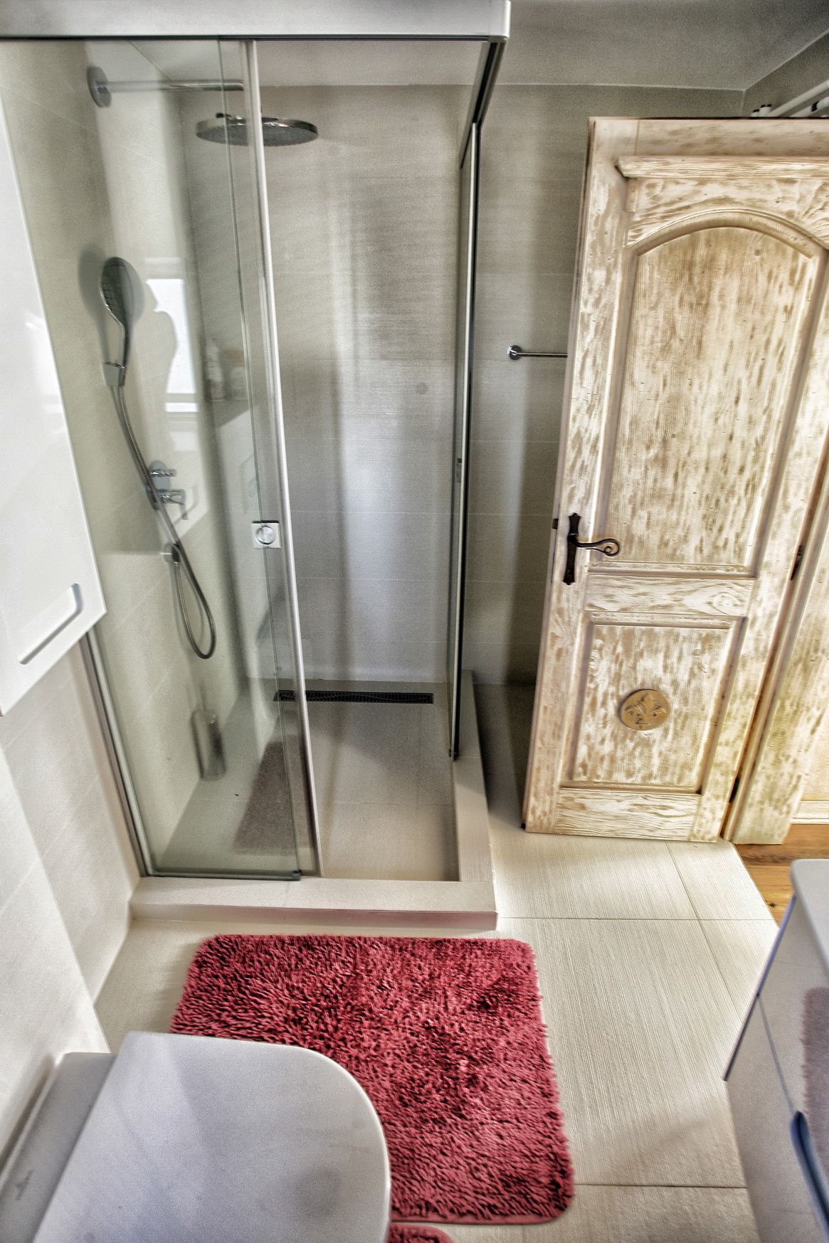 Bathroom in a villa in Reževići, Montenegro: glass shower cabin, light tiles, and a wooden door.