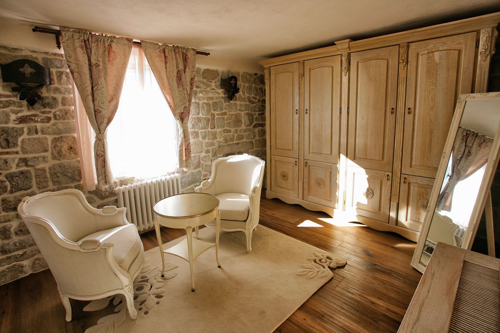 Bedroom interior in a villa in Reževići, Montenegro: stone walls, vintage furniture, a light-colored wardrobe, and a cozy seating area.