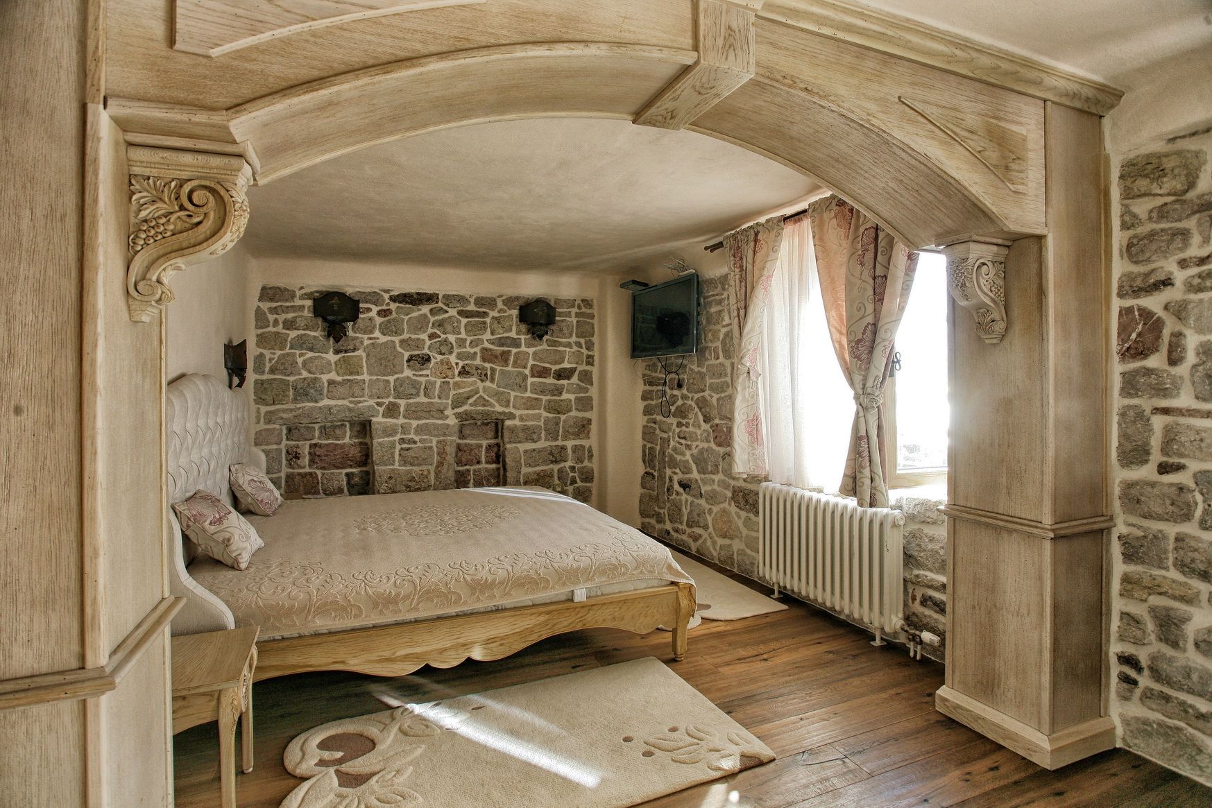 Bedroom in a villa in Rezevici, Montenegro: stone walls, wooden arch, double bed, and parquet flooring.