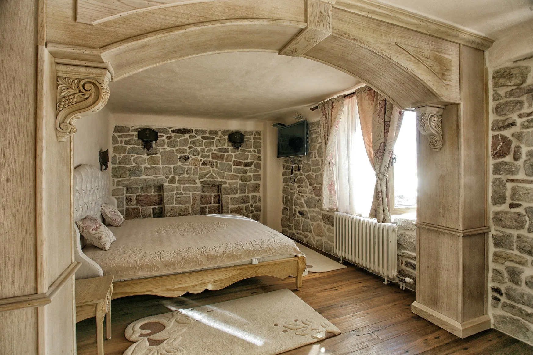 Bedroom with stone walls, wooden arch, and large bed under a carved wooden canopy.