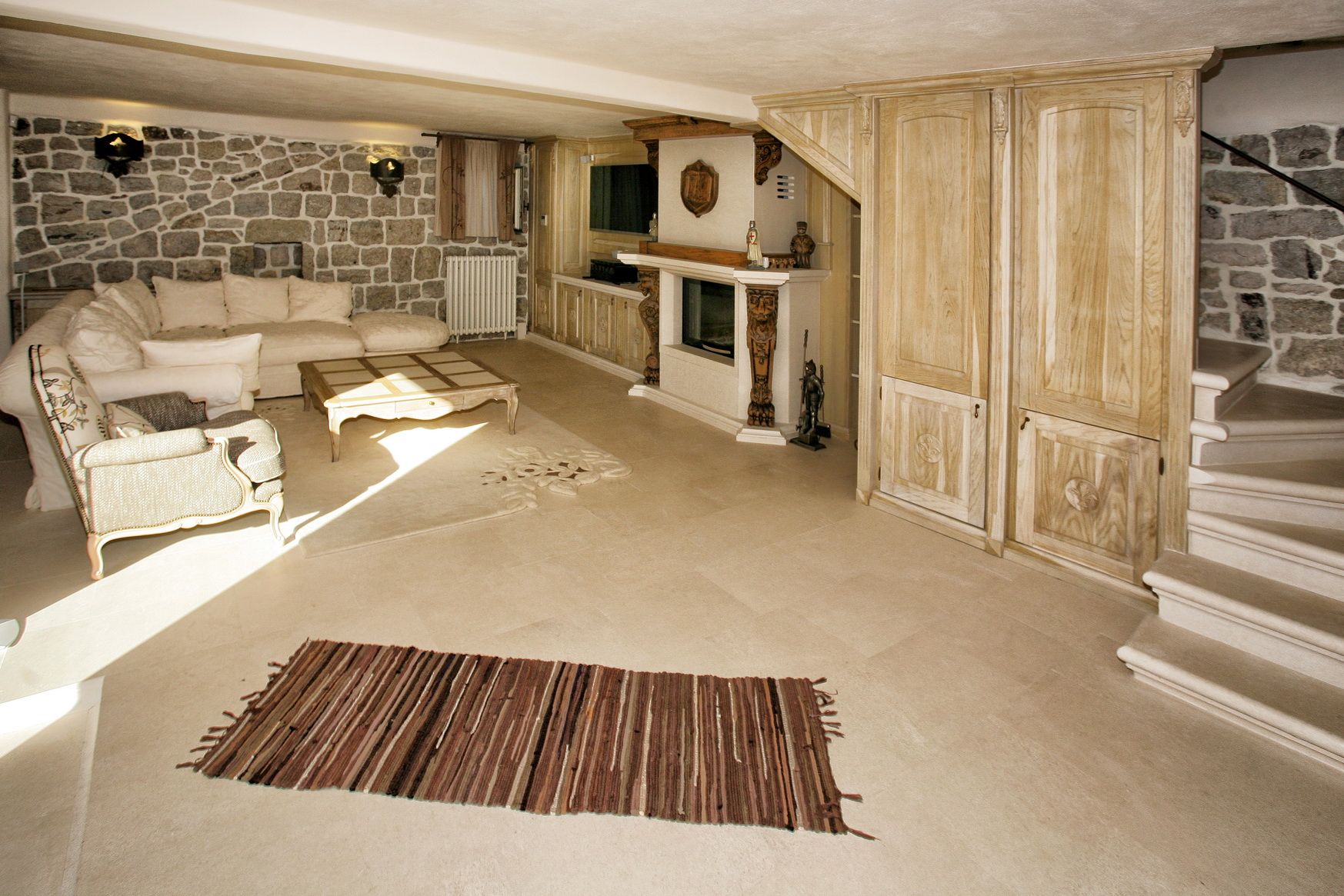 Villa living room in Reževići, Montenegro: stone walls, fireplace, wooden furniture, and a classic-style staircase.