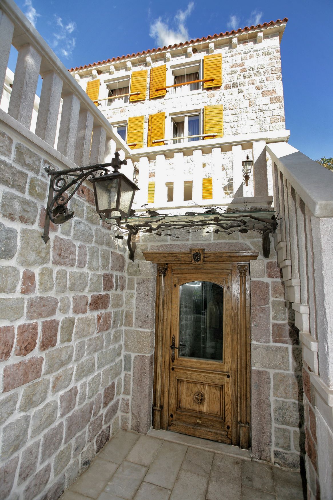 Entrance to a stone Mediterranean-style villa with a wooden door and shutters in Reževići, Montenegro.