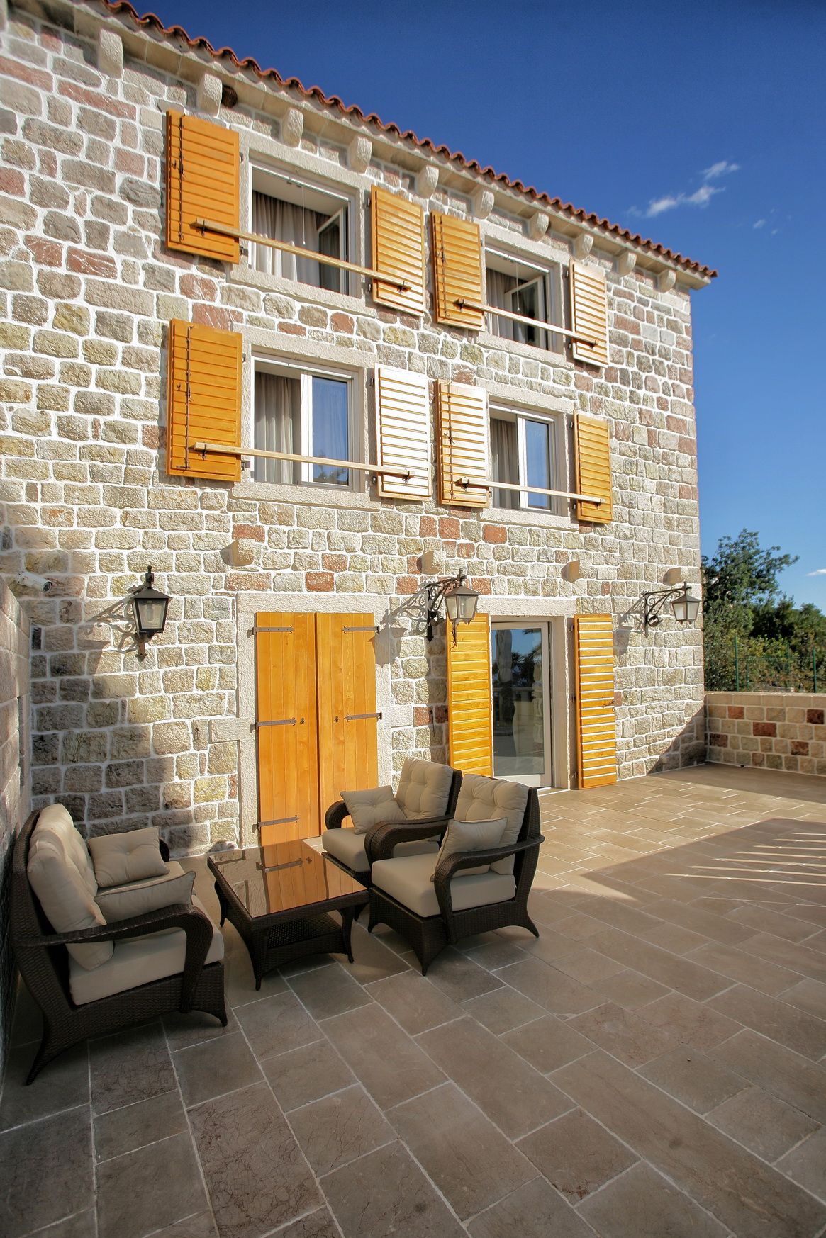 Stone villa in Reževići, Montenegro: terrace with wicker furniture, natural stone facade, and yellow shutters.