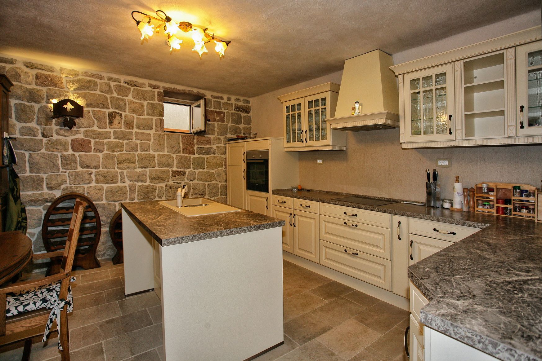 Kitchen with a stone wall and island in a villa in Reževići, Montenegro: a classic interior with beige cabinetry.