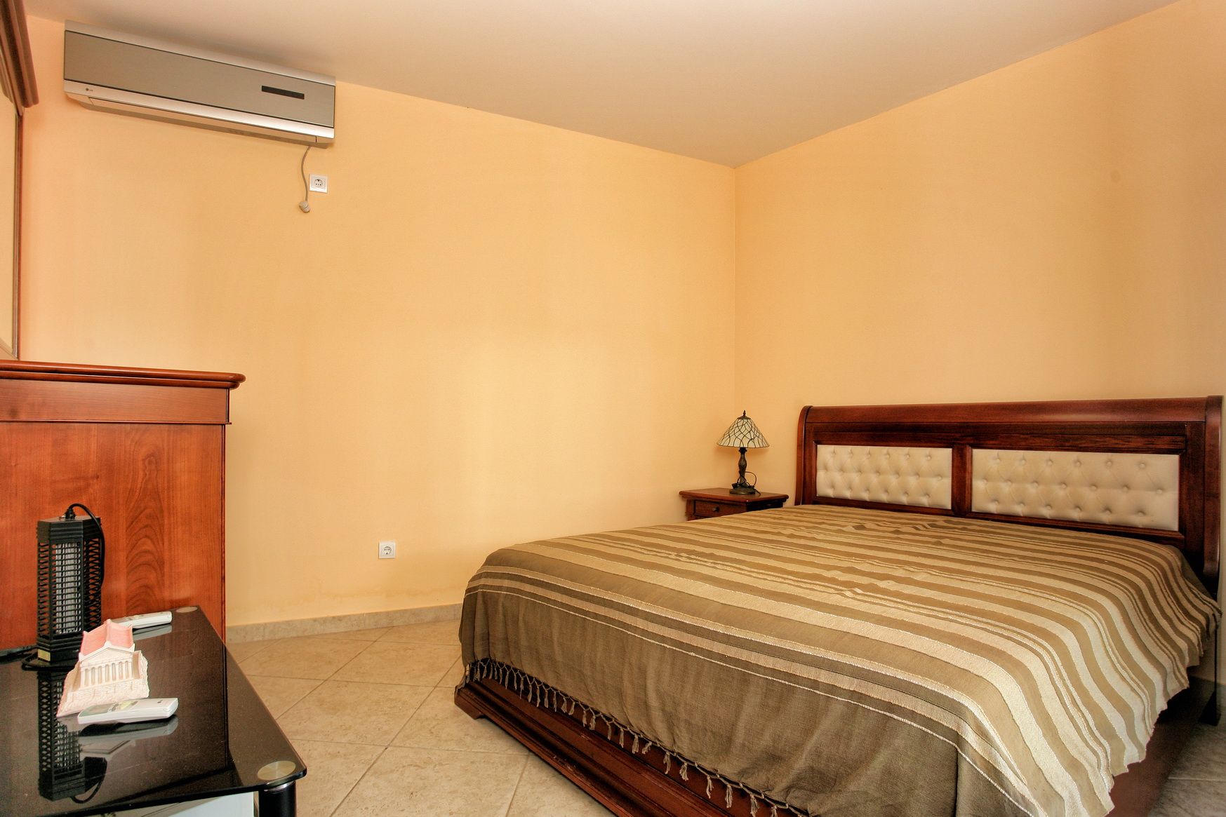Bedroom with a double bed and air conditioning in a villa in Reževići, Montenegro: interior with wooden furniture.