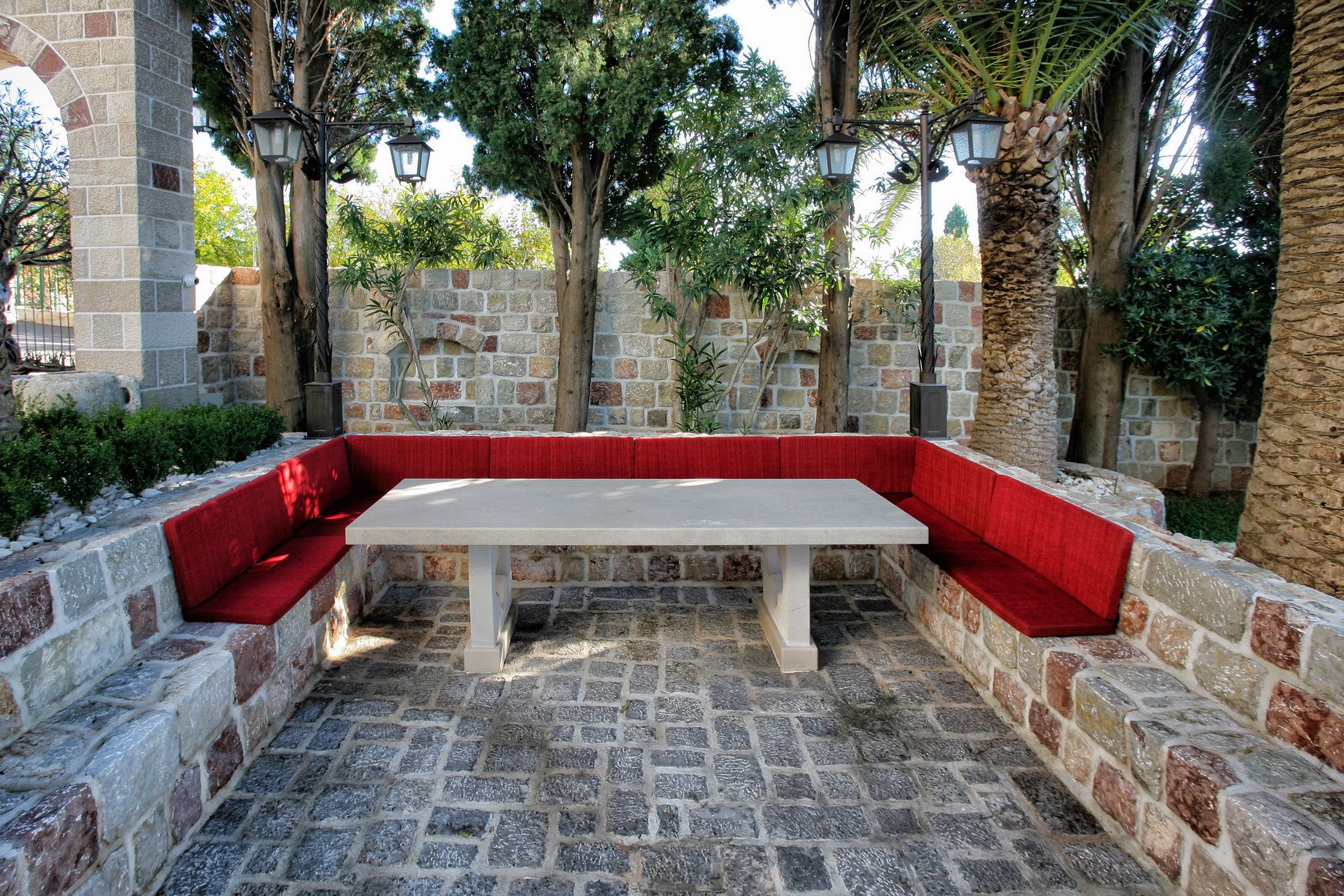 Relaxation area with a stone table and red seating in the villa garden in Reževići, Montenegro, against a stone wall.