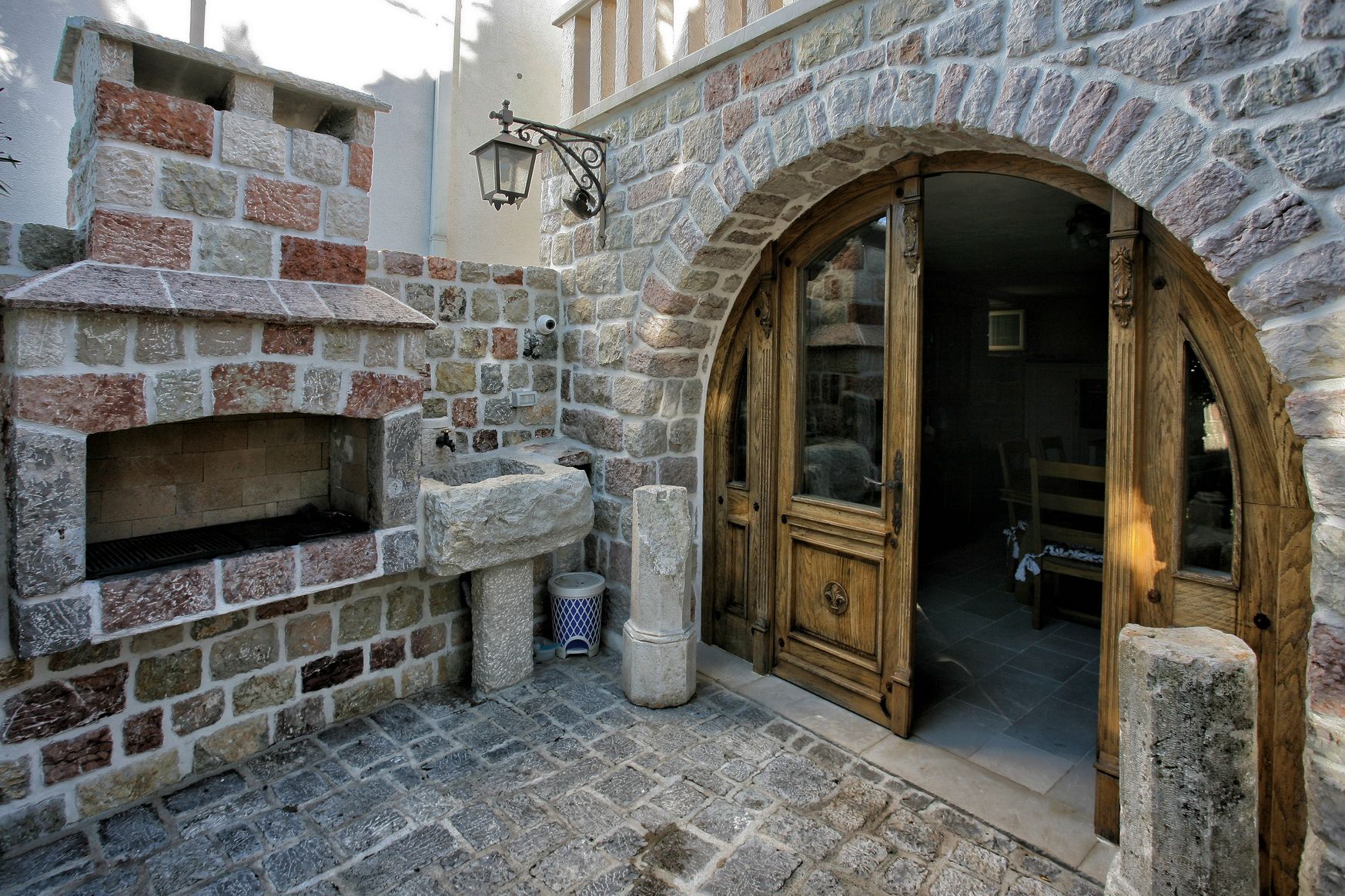 Terrace with a stone barbecue and an arched wooden door of a villa in Reževići, Montenegro. Natural stone finish.