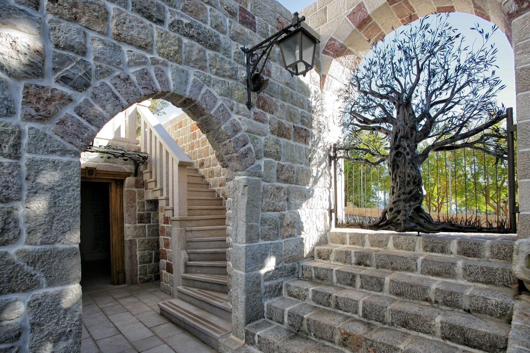 Stone staircase and wrought-iron gates in the shape of a tree at a villa in Reževići, Montenegro. Natural stone architecture.