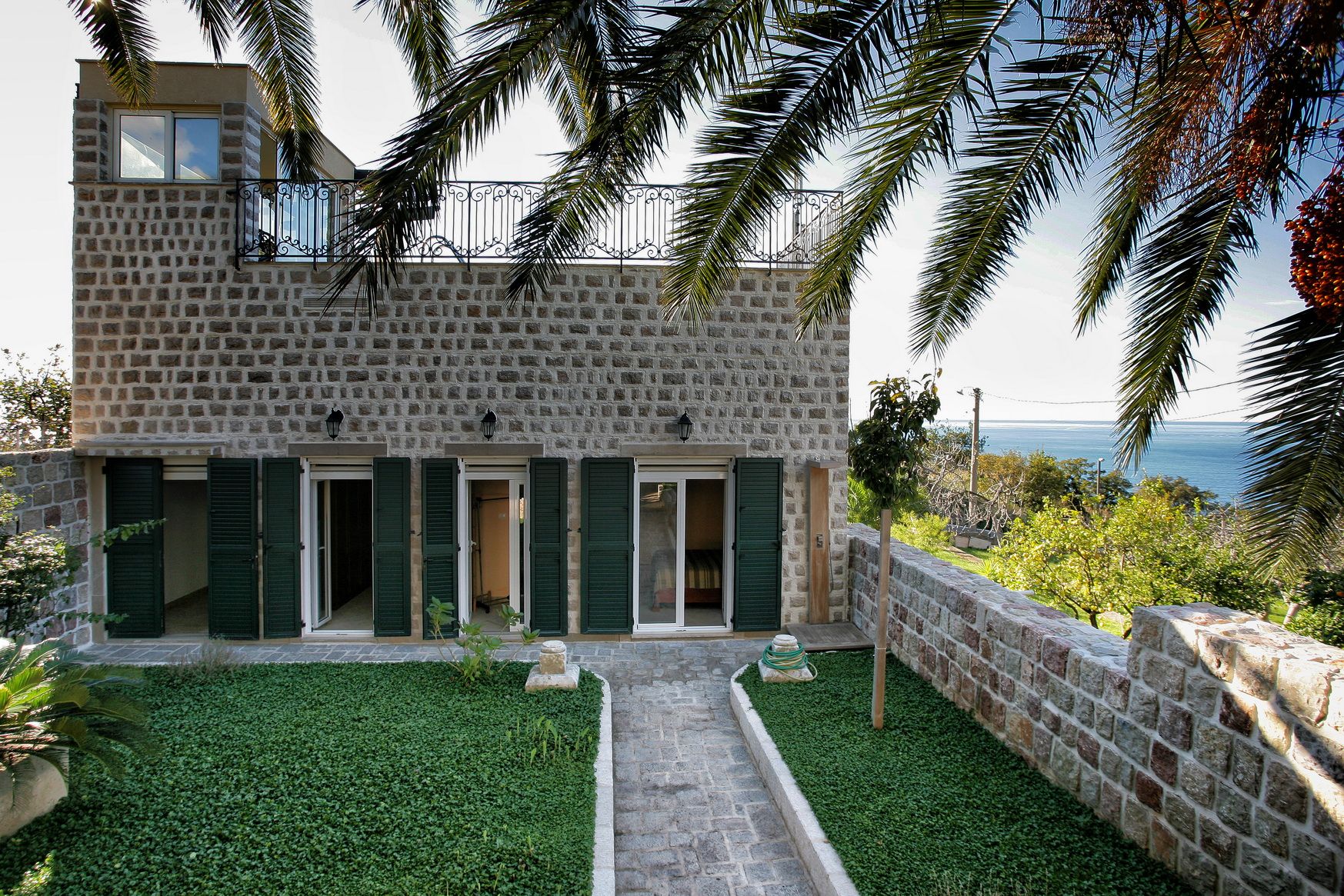 Stone villa in Reževići, Montenegro: facade with a terrace, green garden, and panoramic view of the Adriatic Sea.