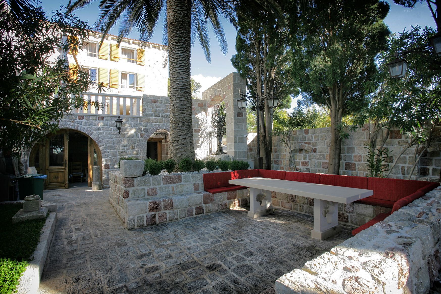 Cozy villa courtyard in Reževići, Montenegro: stone finishes, a palm tree, and a dining area with red seating.