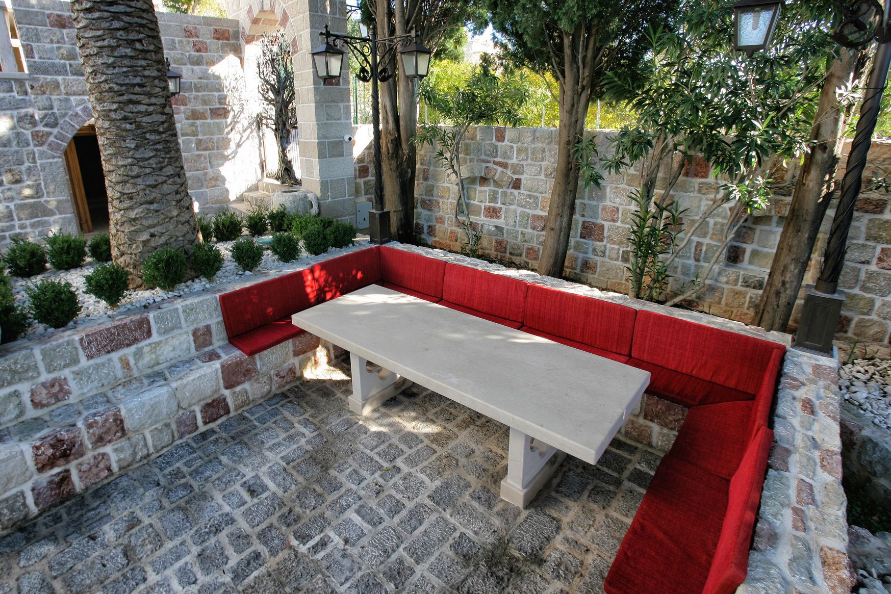 Cozy seating area with a stone table and red seats at a villa in Reževići, Montenegro, surrounded by a garden.