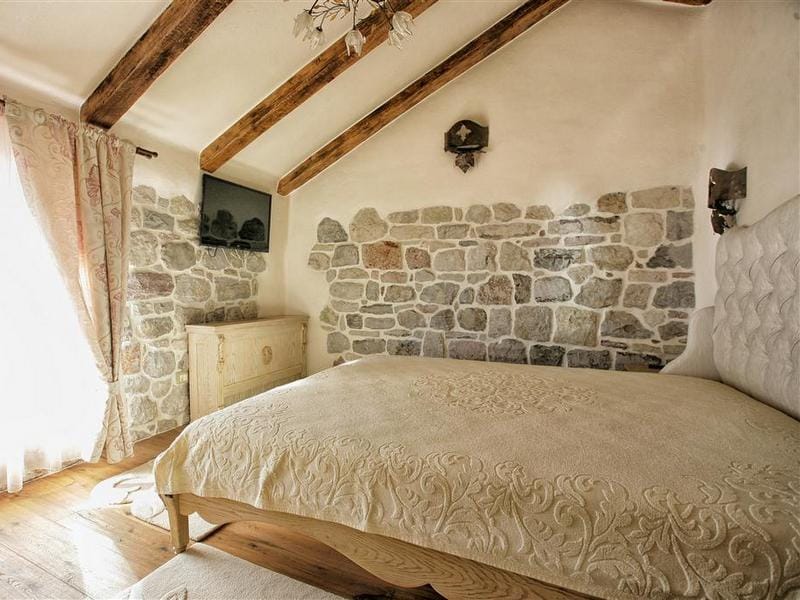 Mediterranean-style bedroom in a villa in Reževići, Montenegro: stonework, wooden beams, and a double bed.