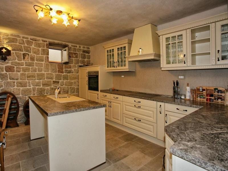 Classic-style kitchen with a stone wall in a villa in Reževići, Montenegro: light cabinetry and an island area.