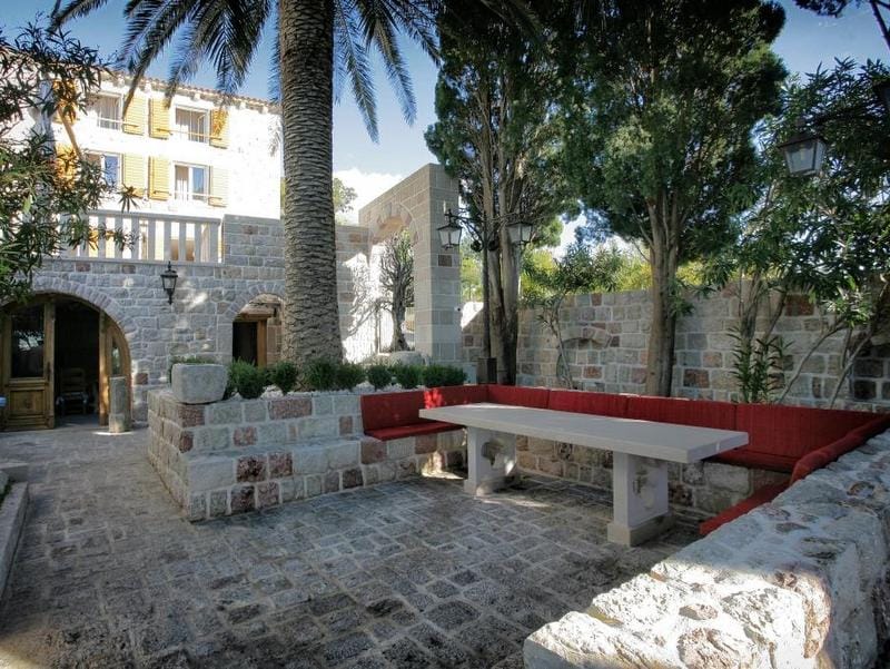 Cozy villa terrace in Reževići, Montenegro: stonework, dining area with red seating, and a palm tree in the courtyard.