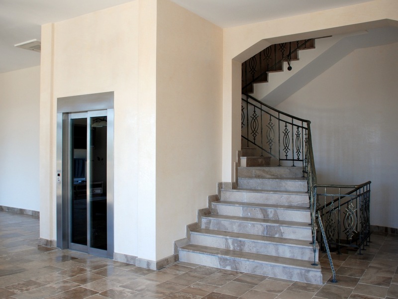 Interior of a villa in Petrovac, Montenegro: a modern elevator and a marble staircase with wrought-iron railings in the hall.