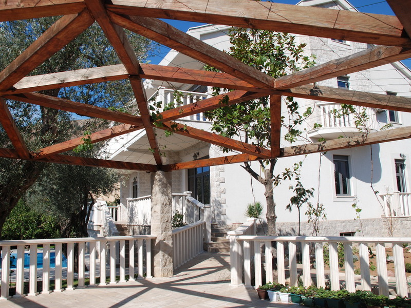Wooden pergola on the terrace of a villa in Petrovac, Montenegro, overlooking the house facade and the garden pool.