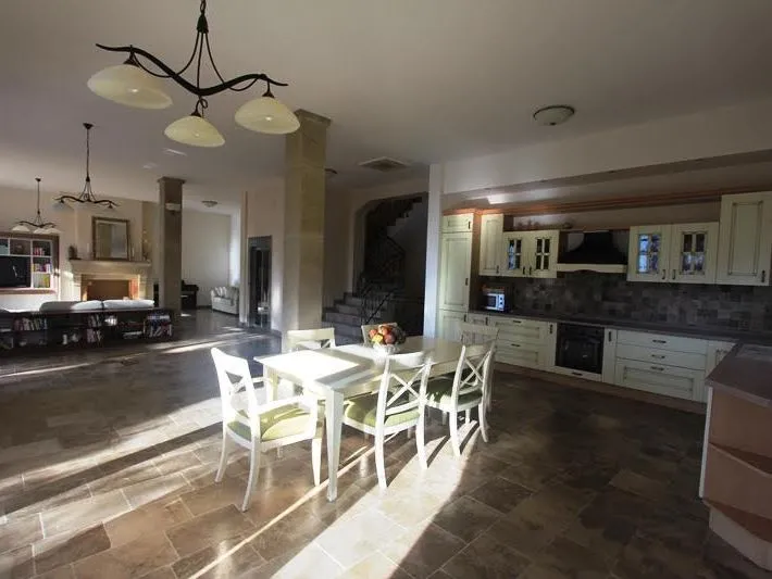 Open plan space featuring a kitchen, white dining set, and living area with fireplace in background.