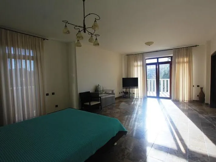 Bedroom featuring a bed with turquoise cover, TV, chandelier, and balcony doors with curtains.