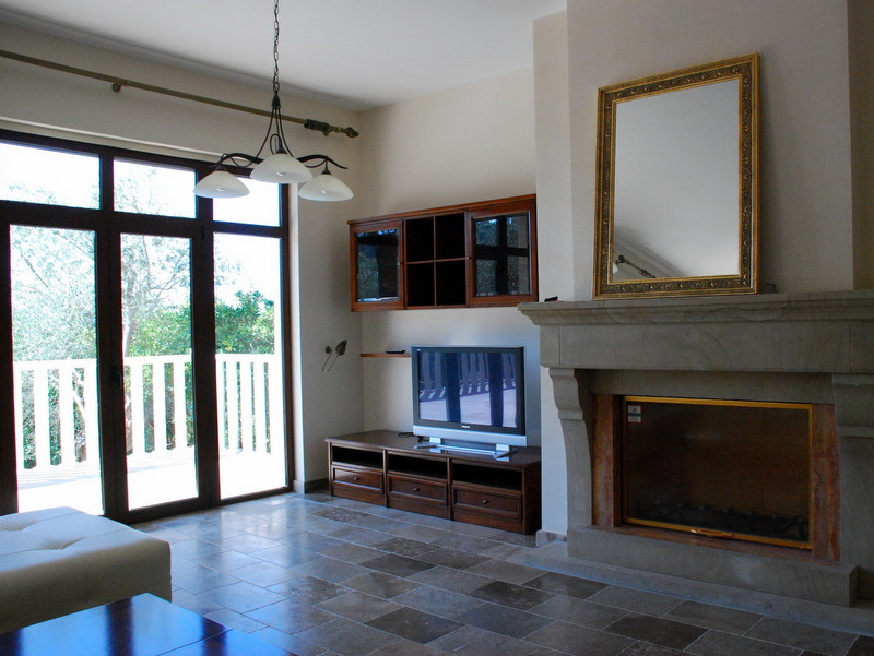 Living room with a fireplace and access to the terrace in a villa, Petrovac, Montenegro: stone floor, TV area, and a framed mirror.