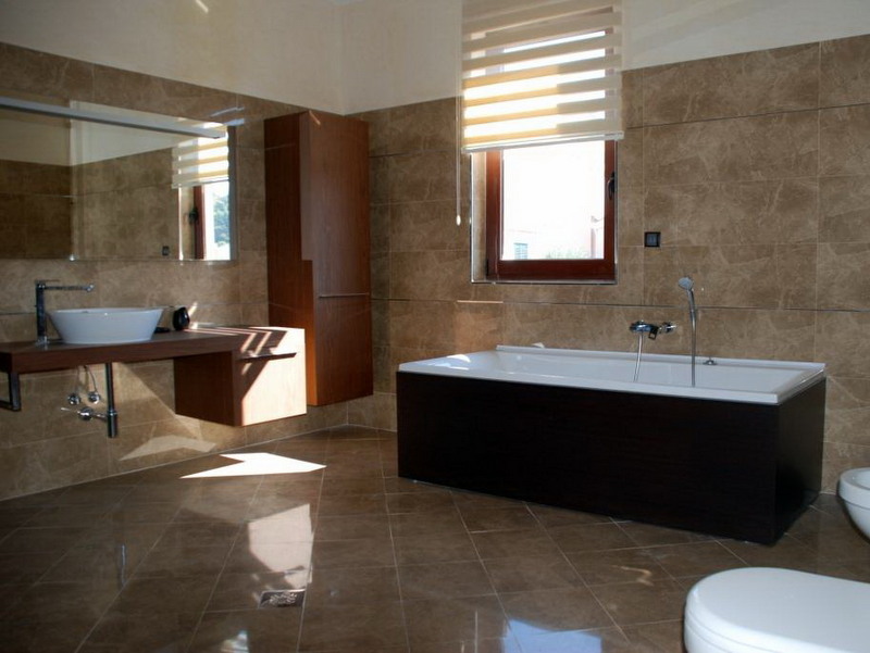 Modern bathroom with brown tiles, a white bathtub, and wooden furniture in a villa in Petrovac, Montenegro.