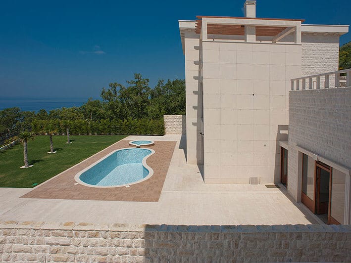 Modern villa in Reževići, Montenegro: stone facade, outdoor pool, landscaped garden, and panoramic sea view.
