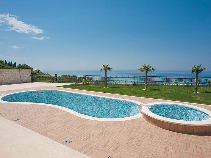 Open-air pool with jacuzzi and sea view at a villa in Reževići, Montenegro: tiled terrace and well-kept lawn.