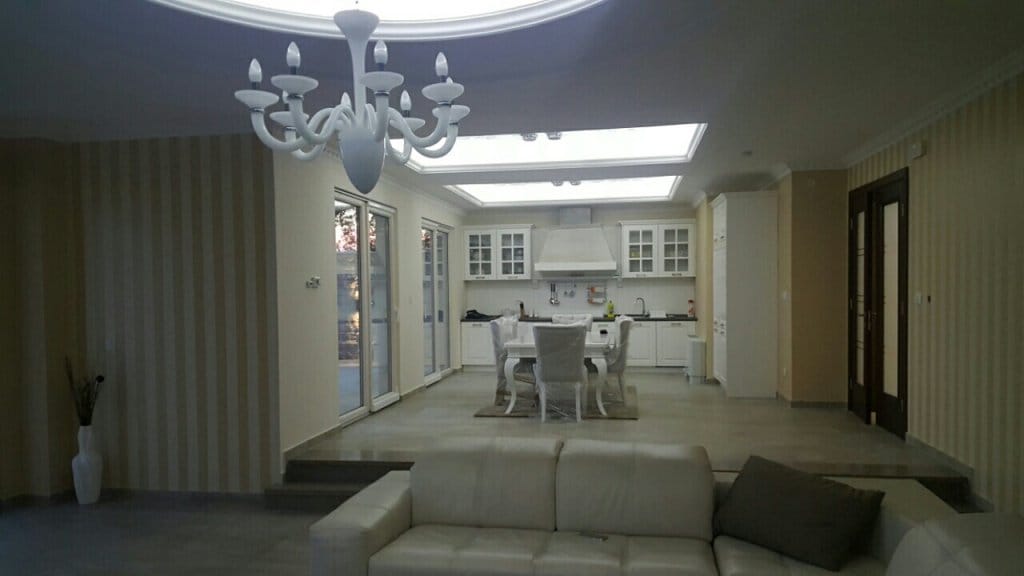 Spacious living room with white furniture and kitchen in a villa in Reževići, Montenegro: modern interior with a chandelier.